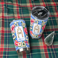 Two Mahjong Tile Number Floral Tumblers lying on a red and green plaid fabric beside a small decorative pine tree.