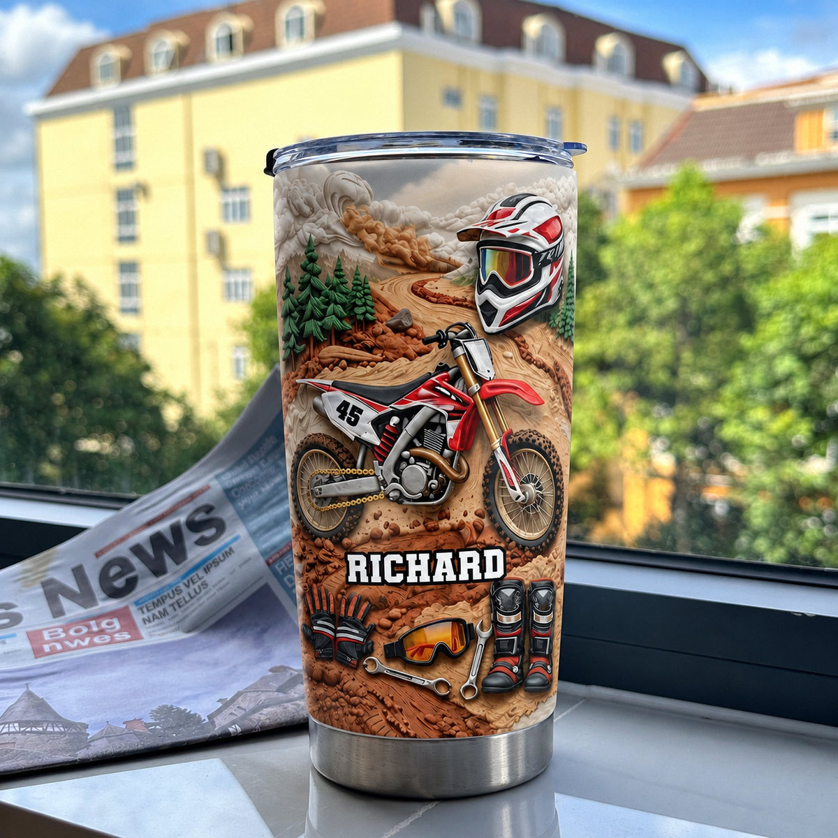 Stainless steel insulated tumbler featuring red dirt bike design standing on windowsill with newspaper beside it.