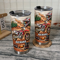 Two custom name dirt bike tumblers sitting on wicker coaster with white tile wall behind them.