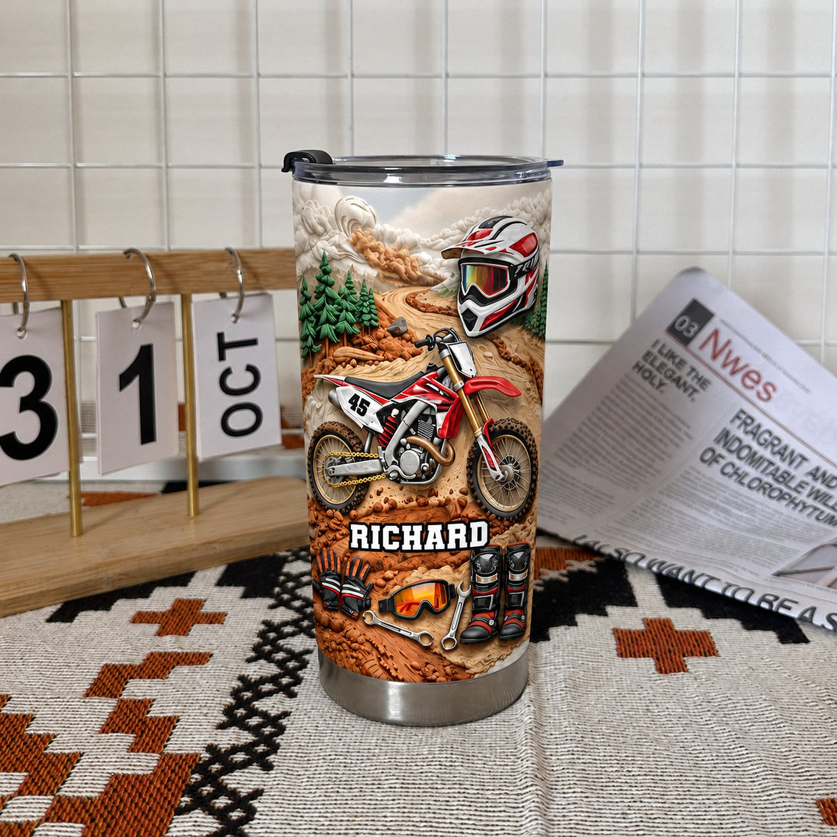 Personalized motocross tumbler on patterned table mat next to small calendar and newspaper.