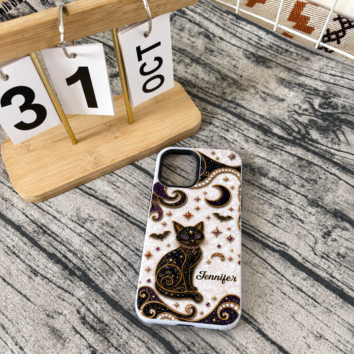 Personalized black cat phone case with white textured background placed next to a wooden desk calendar.