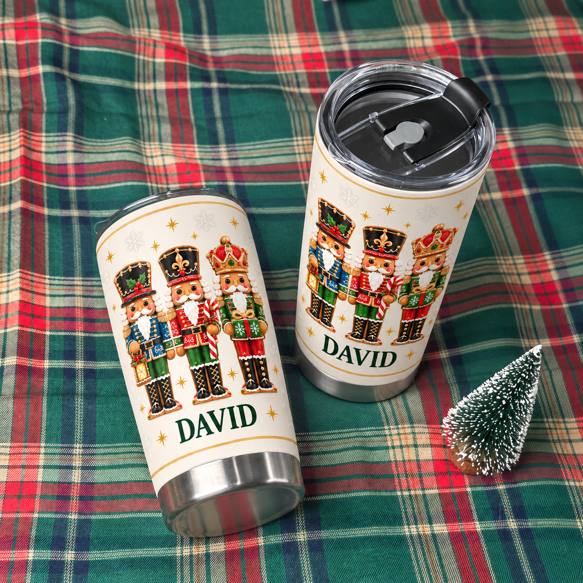 Two personalized white stainless steel nutcracker Christmas tumblers with name David laid on red and green plaid blanket