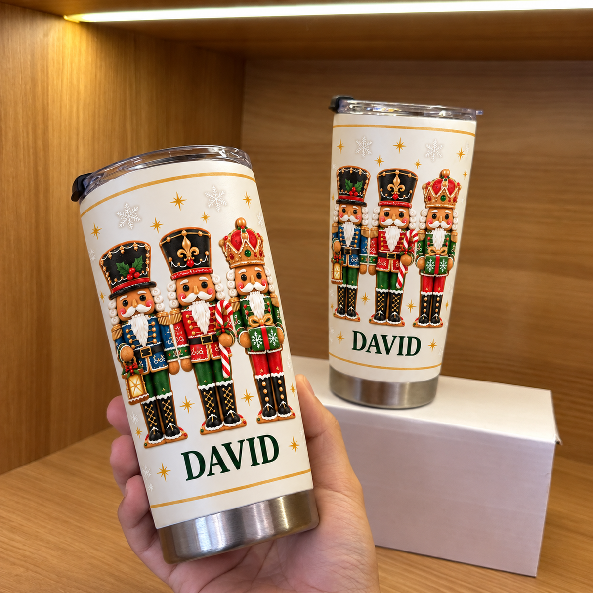 Hand holding white stainless steel nutcracker Christmas tumbler with custom name David on wooden shelf next to box