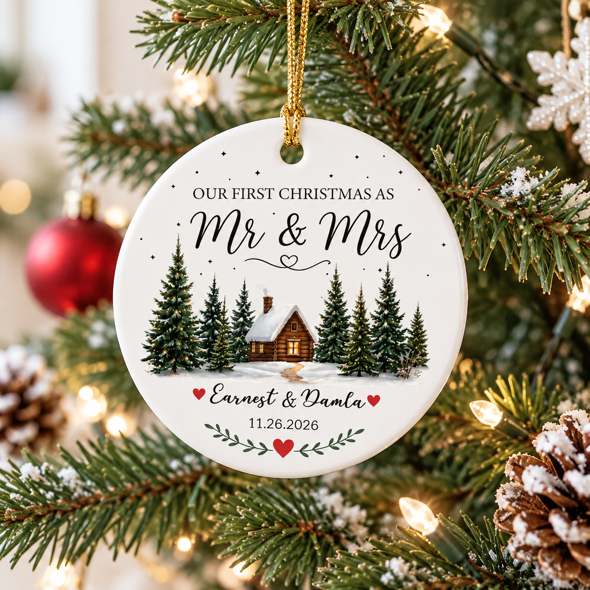 Mr & Mrs ornament hanging on a Christmas tree with snowy pine branches, lights, and a pinecone.