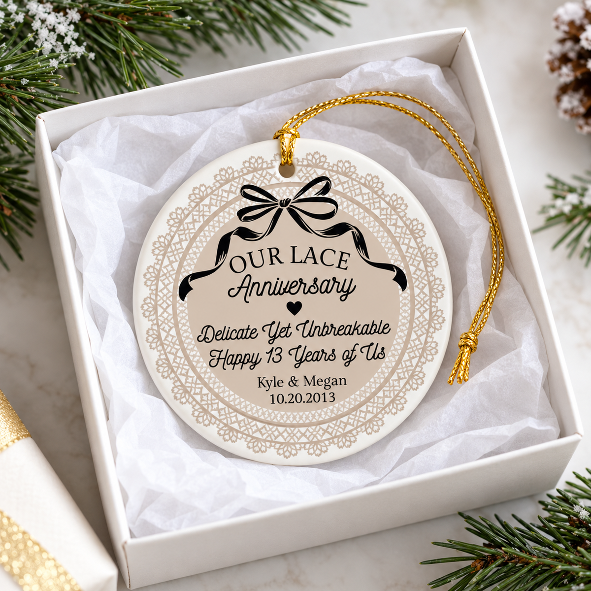 Round ceramic lace anniversary ornament nestled in a white gift box with tissue paper and pine sprigs for a couple's gift.