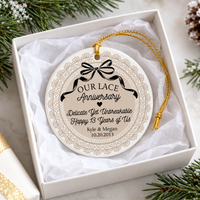 Round ceramic lace anniversary ornament nestled in a white gift box with tissue paper and pine sprigs for a couple's gift.