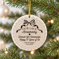 Lace anniversary ornament hanging on a pine tree with a beige lace border, black bow, and personalized couple names.