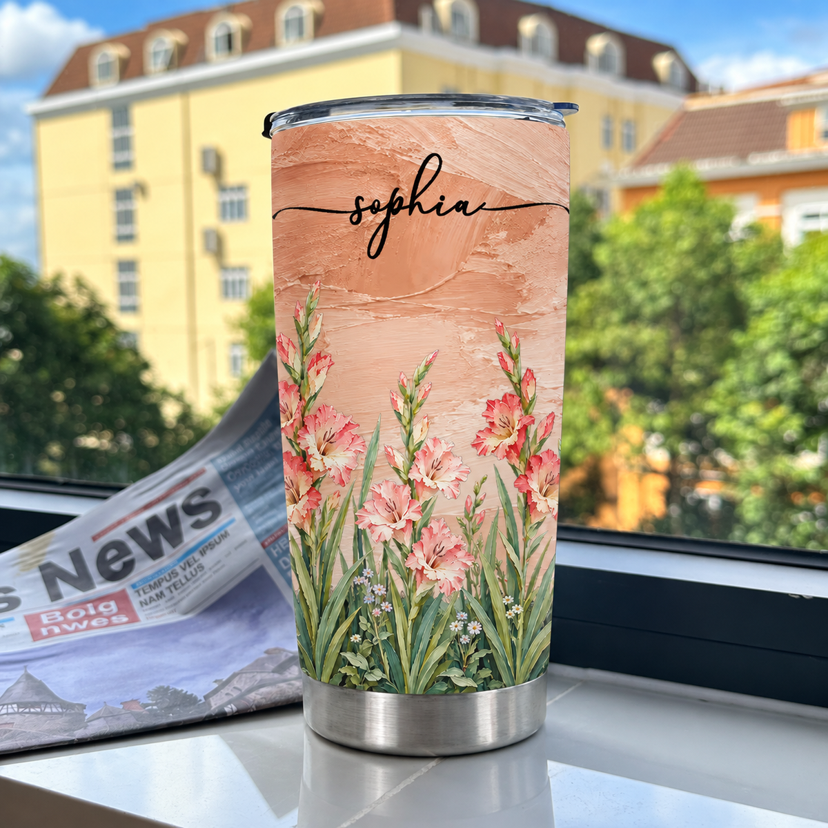 A personalized birth flower tumbler featuring pastel peach background and name Sophia sitting on a windowsill near a