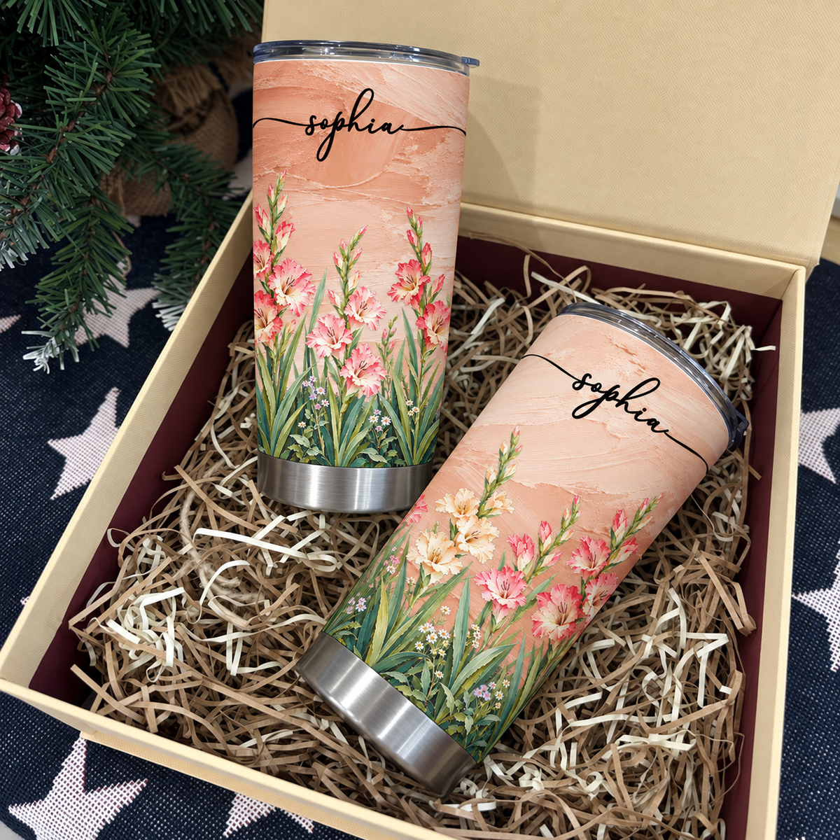 Two personalized birth flower tumblers displayed inside an open gift box filled with shredded paper filler.