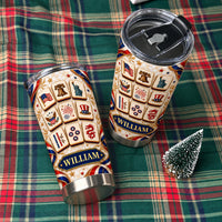 Two personalized patriotic mahjong tiles tumblers with black lids resting on a green plaid blanket next to a tiny pine tree.