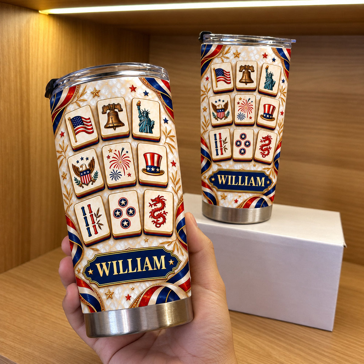 Hand holding a custom name patriotic mahjong tiles tumbler in front of a warm wooden shelf and white box.