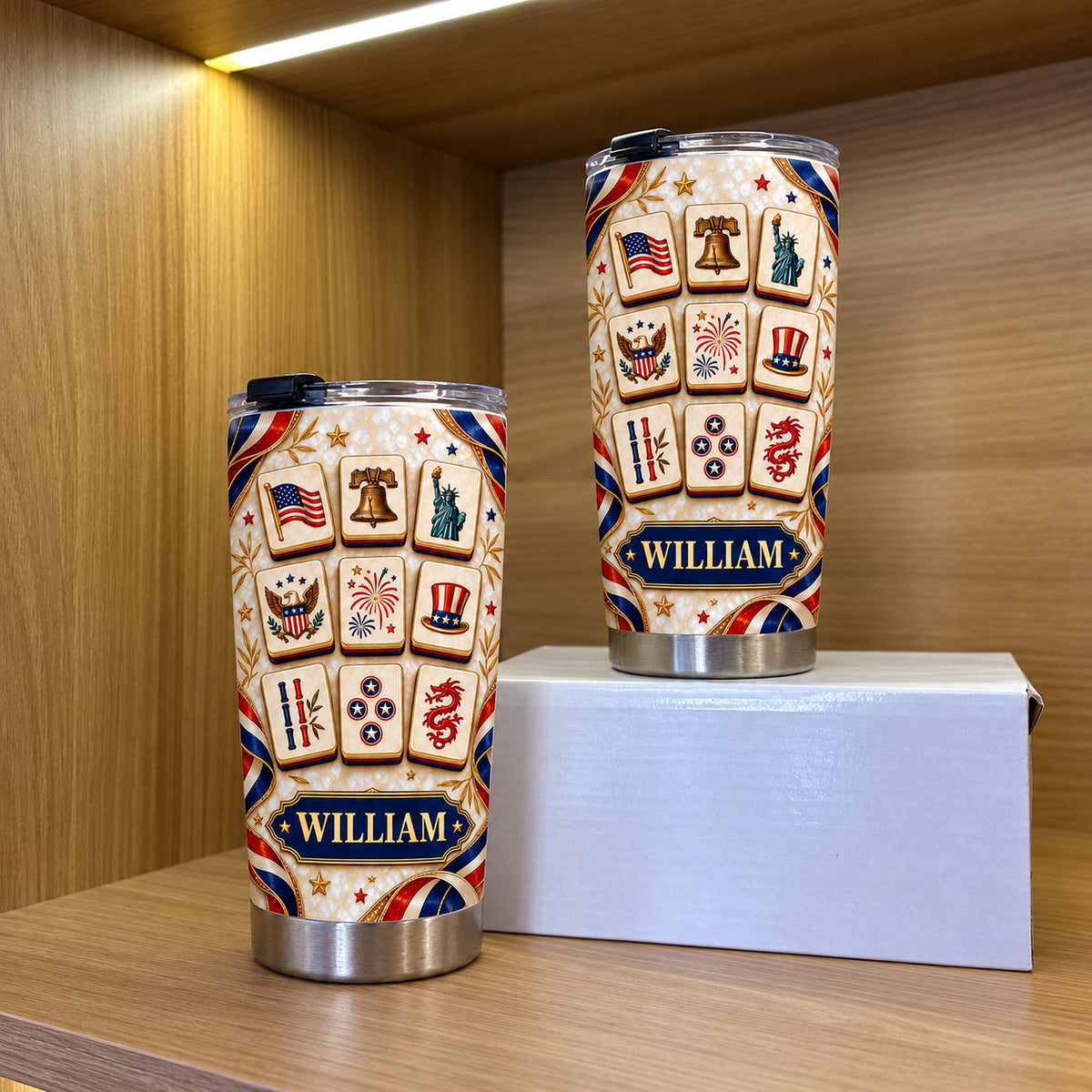 Two stainless steel patriotic mahjong tiles tumblers displayed upright on a white box on a wooden shelf.