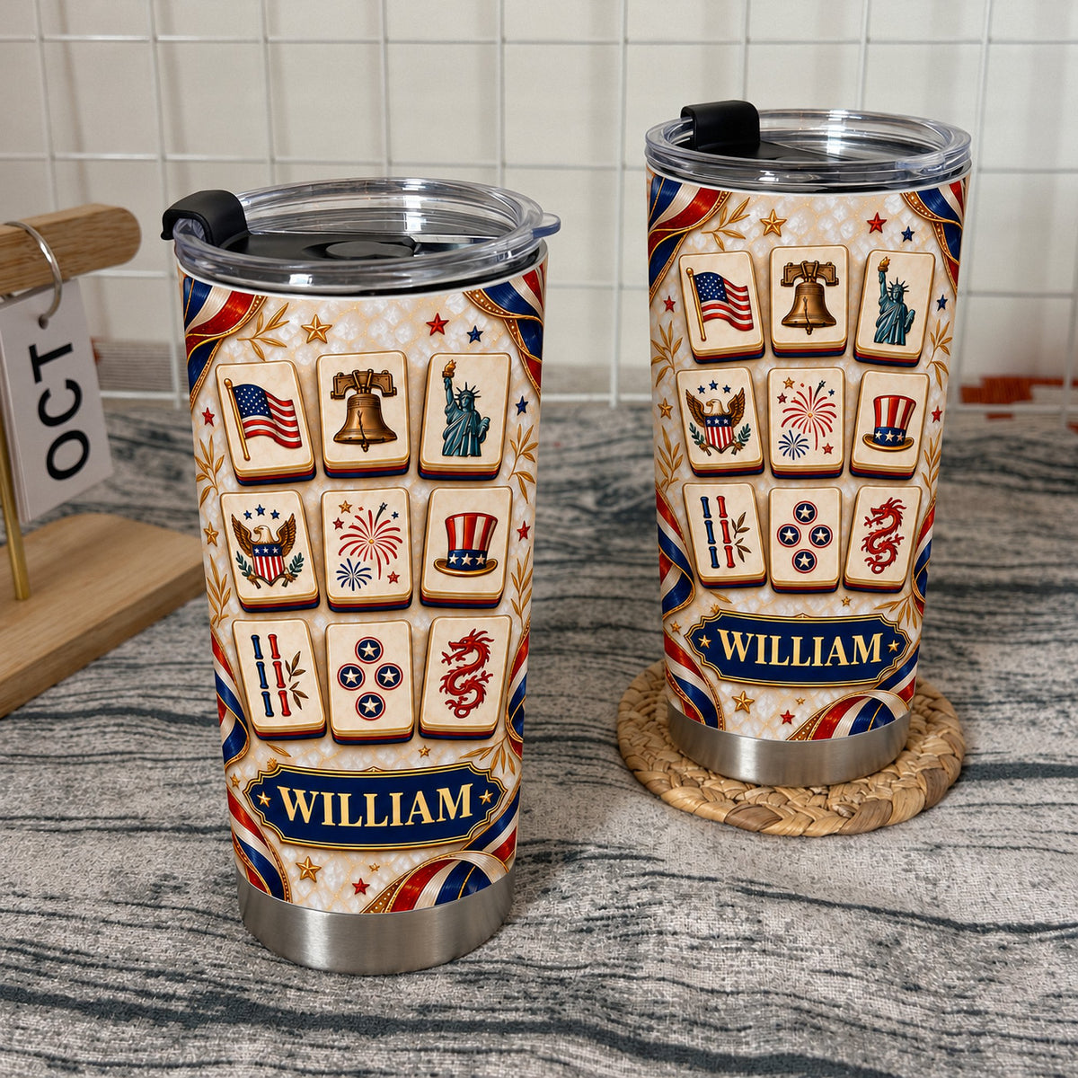 Two patriotic mahjong tiles tumblers with black lids on a woven coaster and wire grid background with an October calendar
