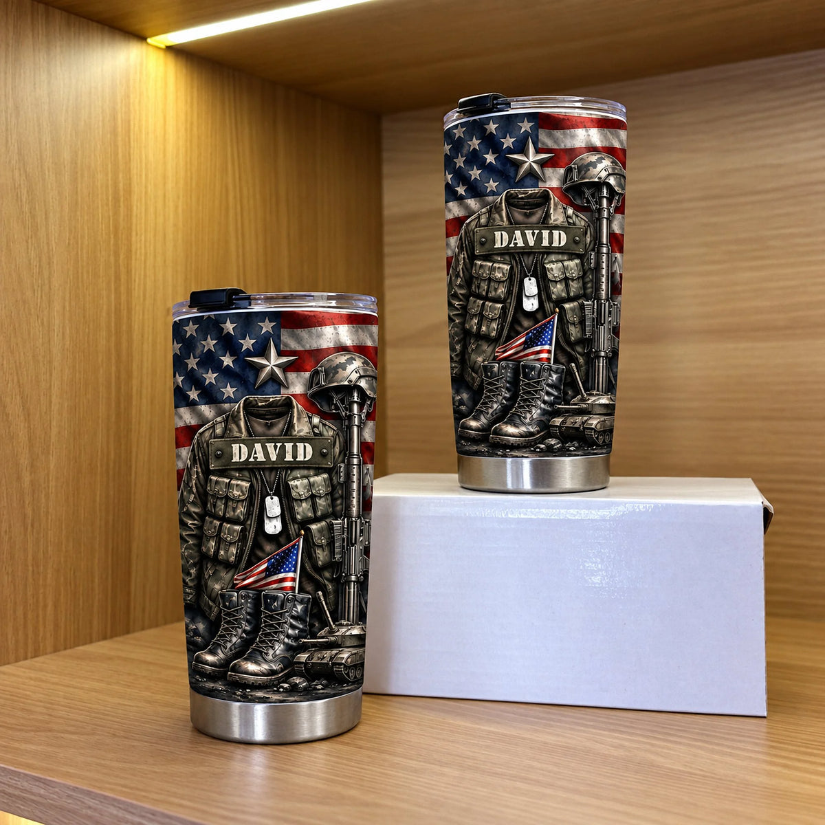 Two patriotic military veteran tumblers of different sizes displayed on a wooden shelf in front of a white box.