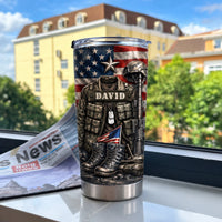 A camouflage tumbler with an American flag background resting on a windowsill with a newspaper and buildings outside.
