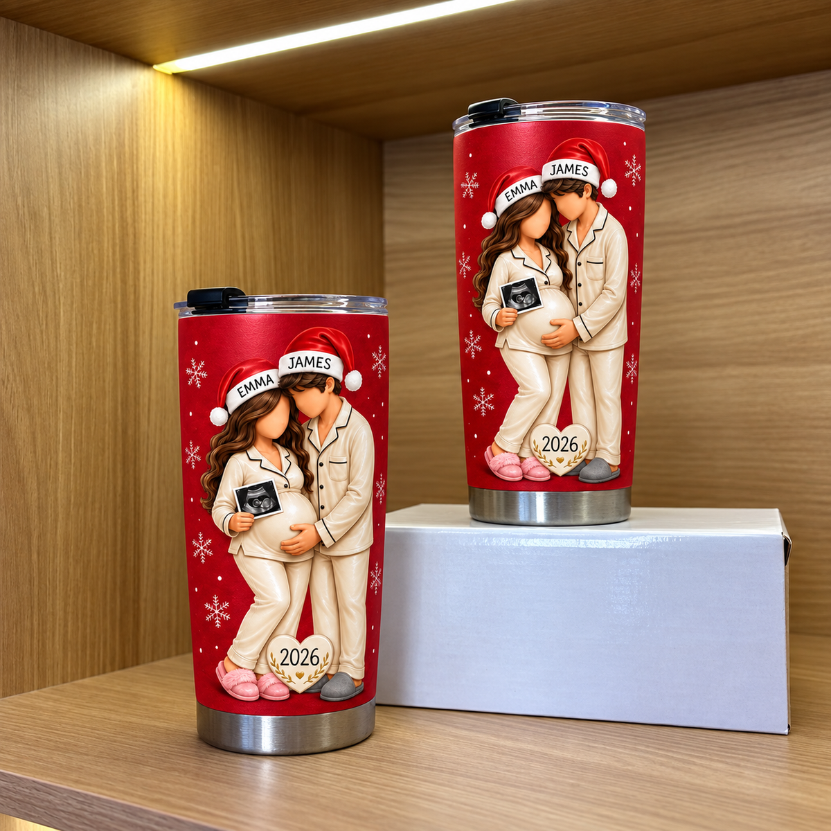 Two red custom name pregnancy tumblers featuring expecting parents in Santa hats on a white box shelf.