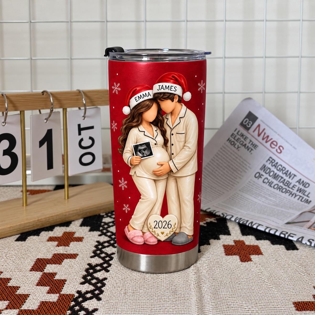 Red custom name tumbler with expecting parents illustration on a patterned mat beside a calendar.