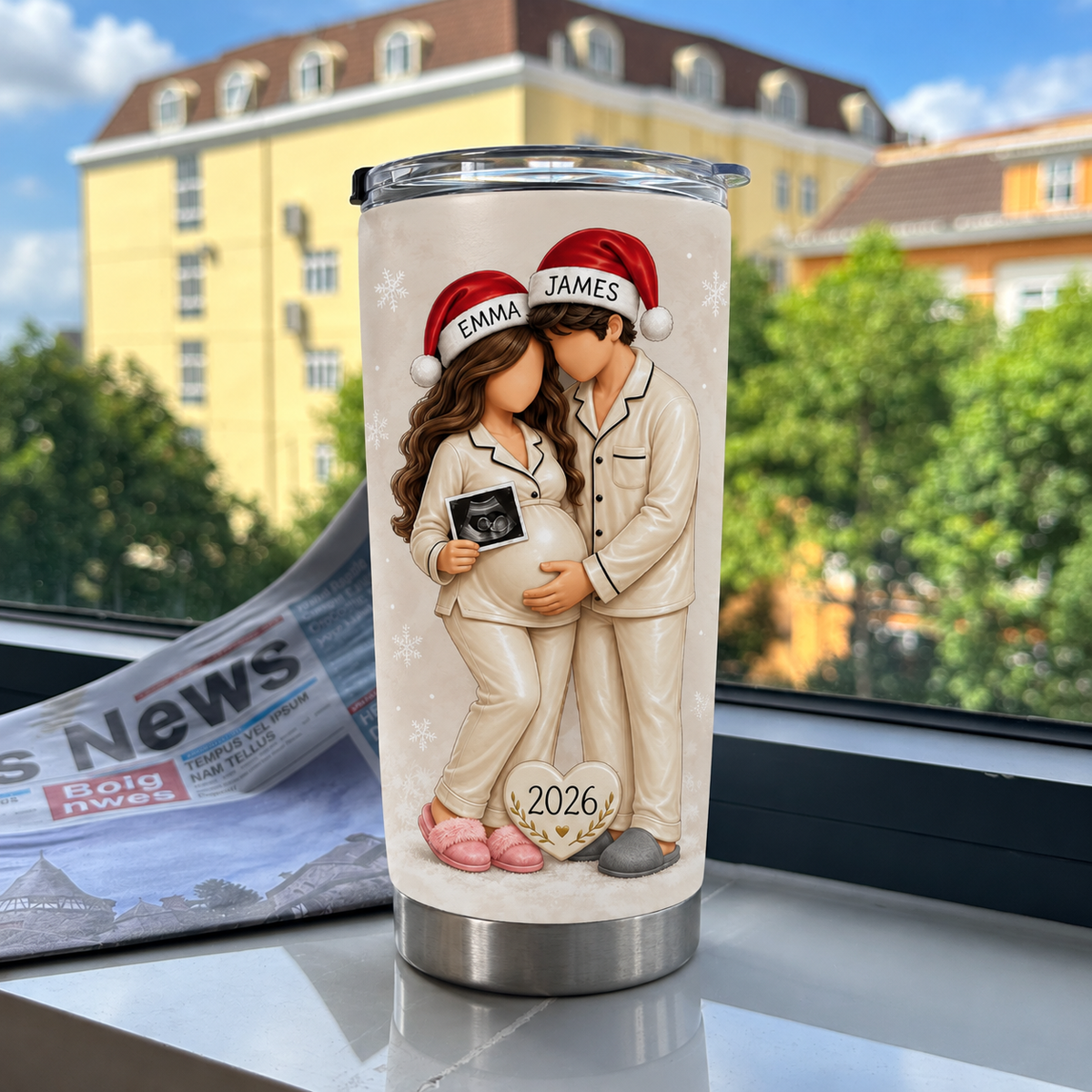 Cream personalized Christmas pregnancy tumbler on a windowsill with a newspaper and buildings outside.