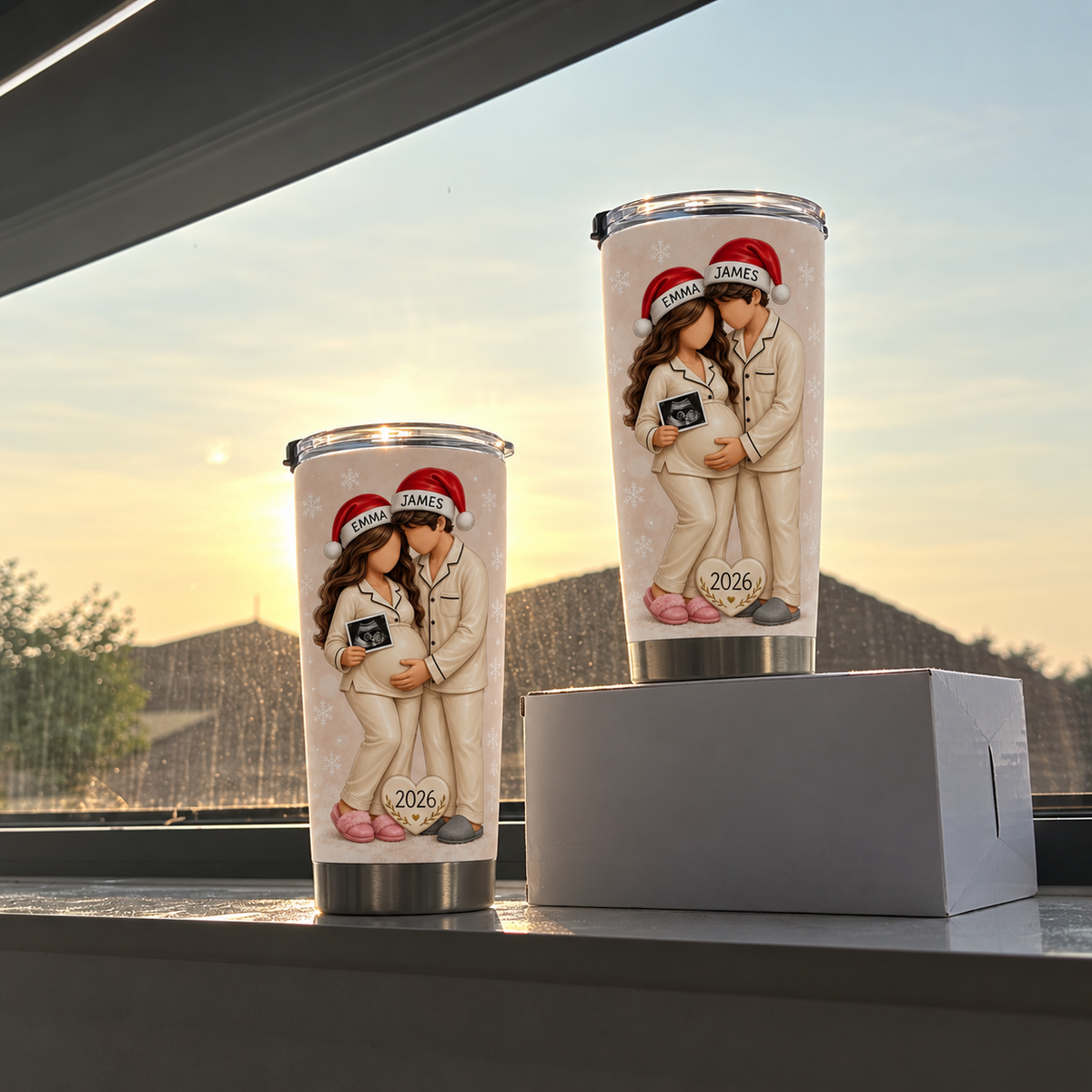 Two cream custom name pregnancy tumblers in different sizes displayed against a sunset window backdrop.