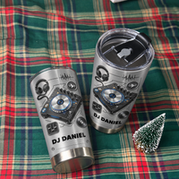 Two personalized DJ tumblers resting on a green and red plaid blanket beside a miniature tree.