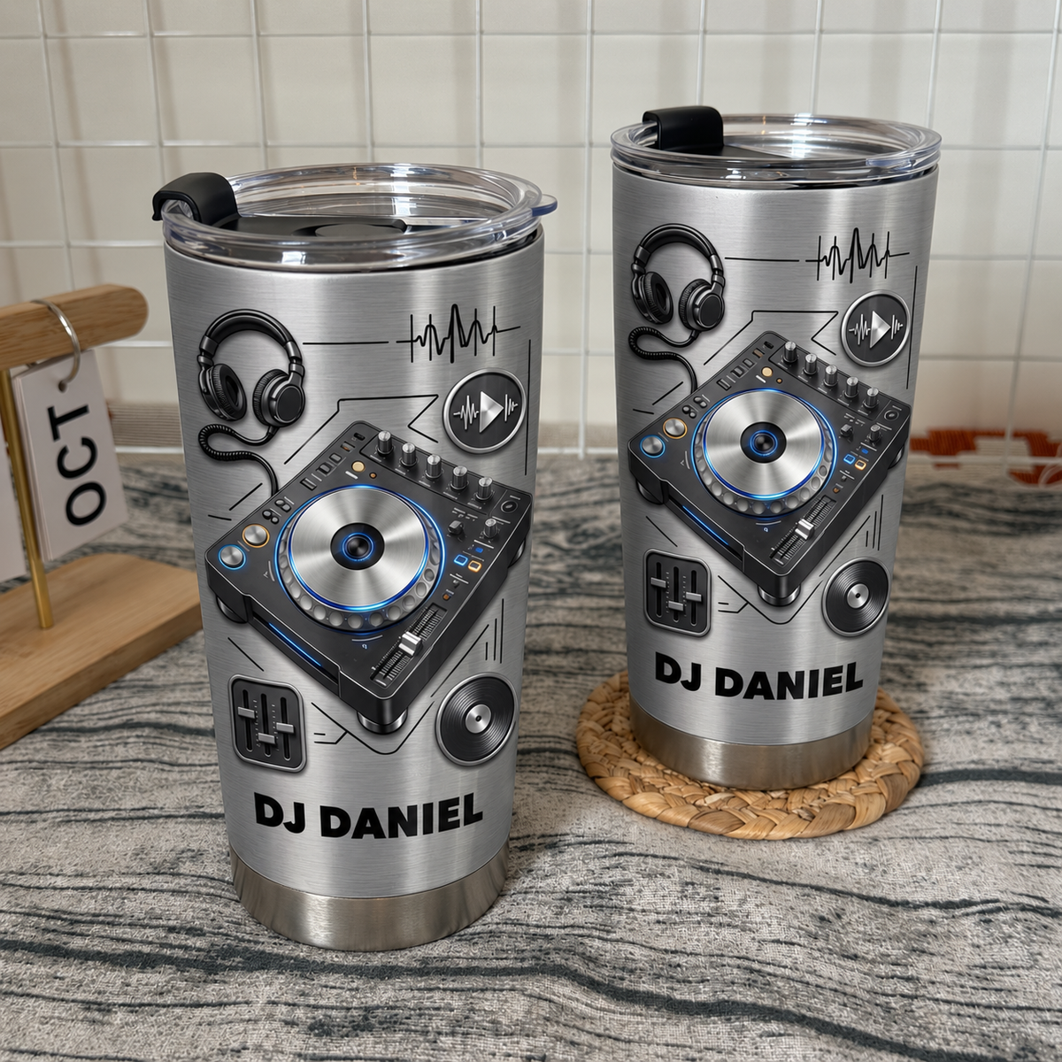 Two stainless steel DJ tumblers with custom names standing on a rustic wooden surface with grid wall.