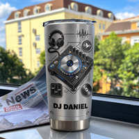 Personalized DJ tumbler on a window sill next to a newspaper with a brushed silver metallic finish.