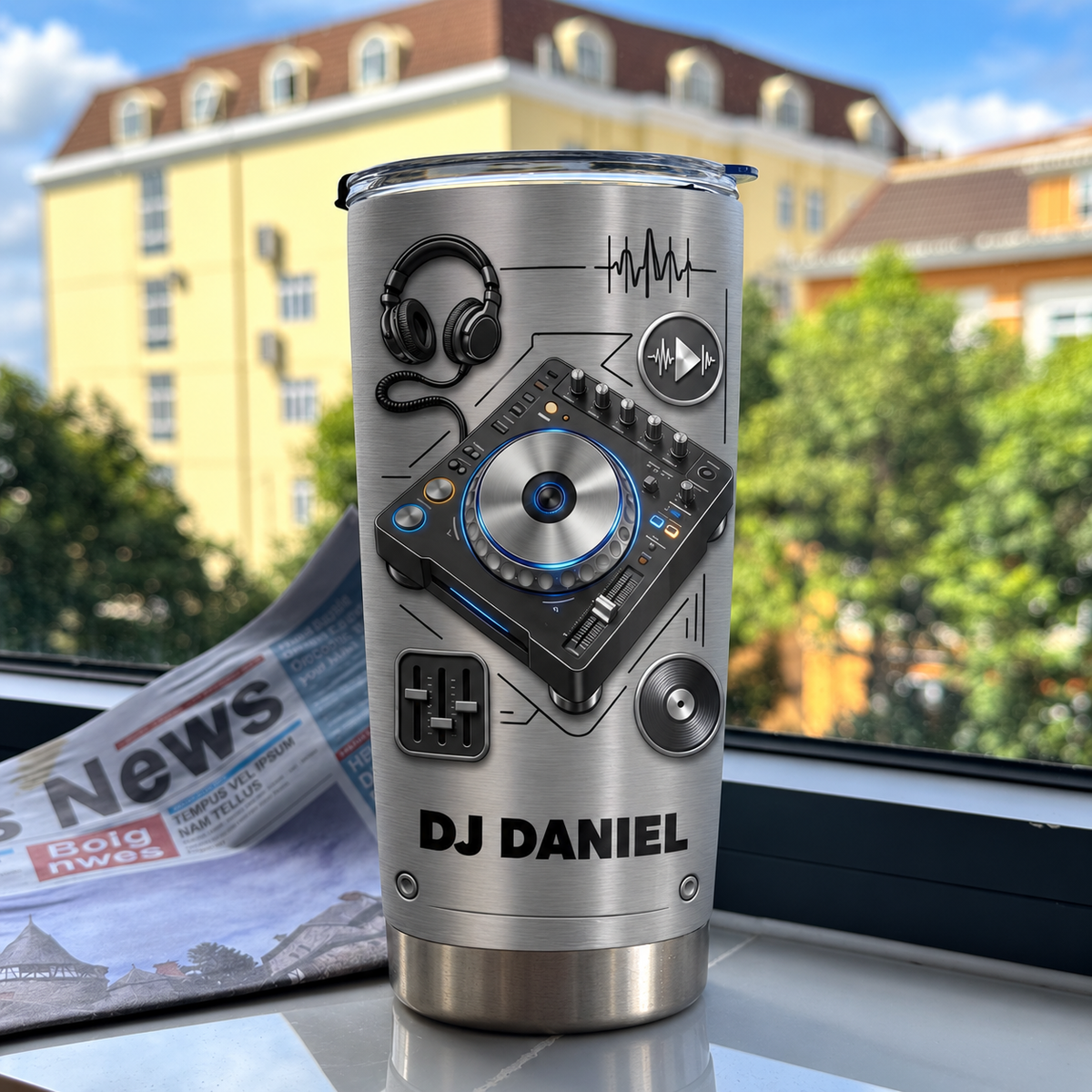 Personalized DJ tumbler on a window sill next to a newspaper with a brushed silver metallic finish.
