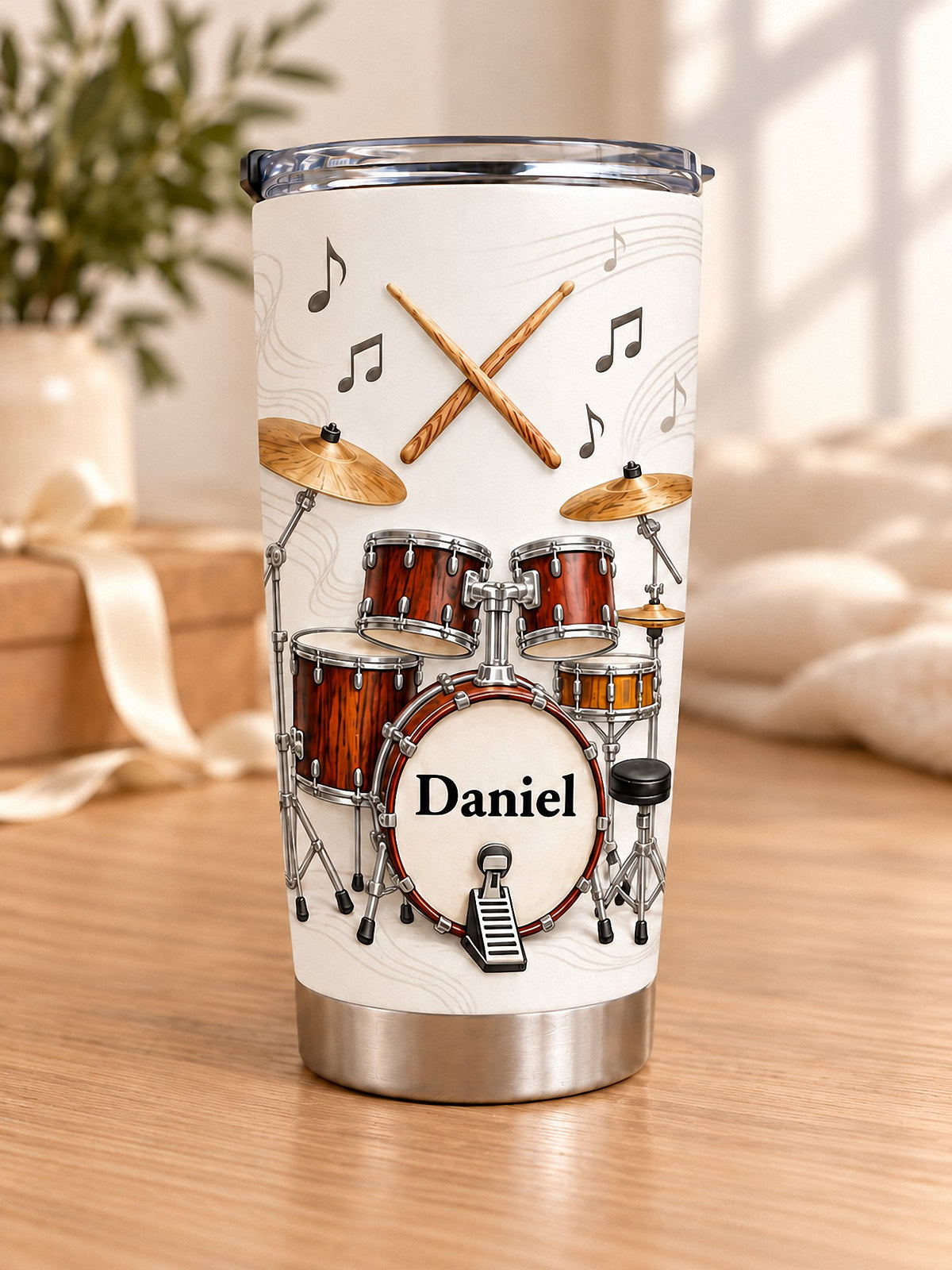 Personalized drum kit tumbler with red wood grain drums and custom name Daniel on wooden surface near window.