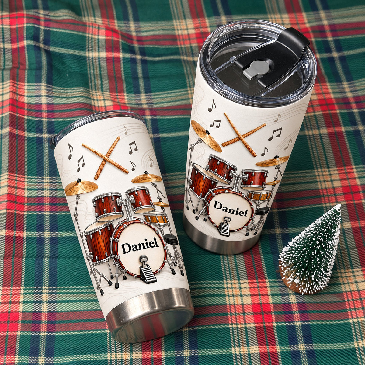 Two personalized drum kit tumblers with custom name Daniel displayed on red and green plaid holiday blanket.