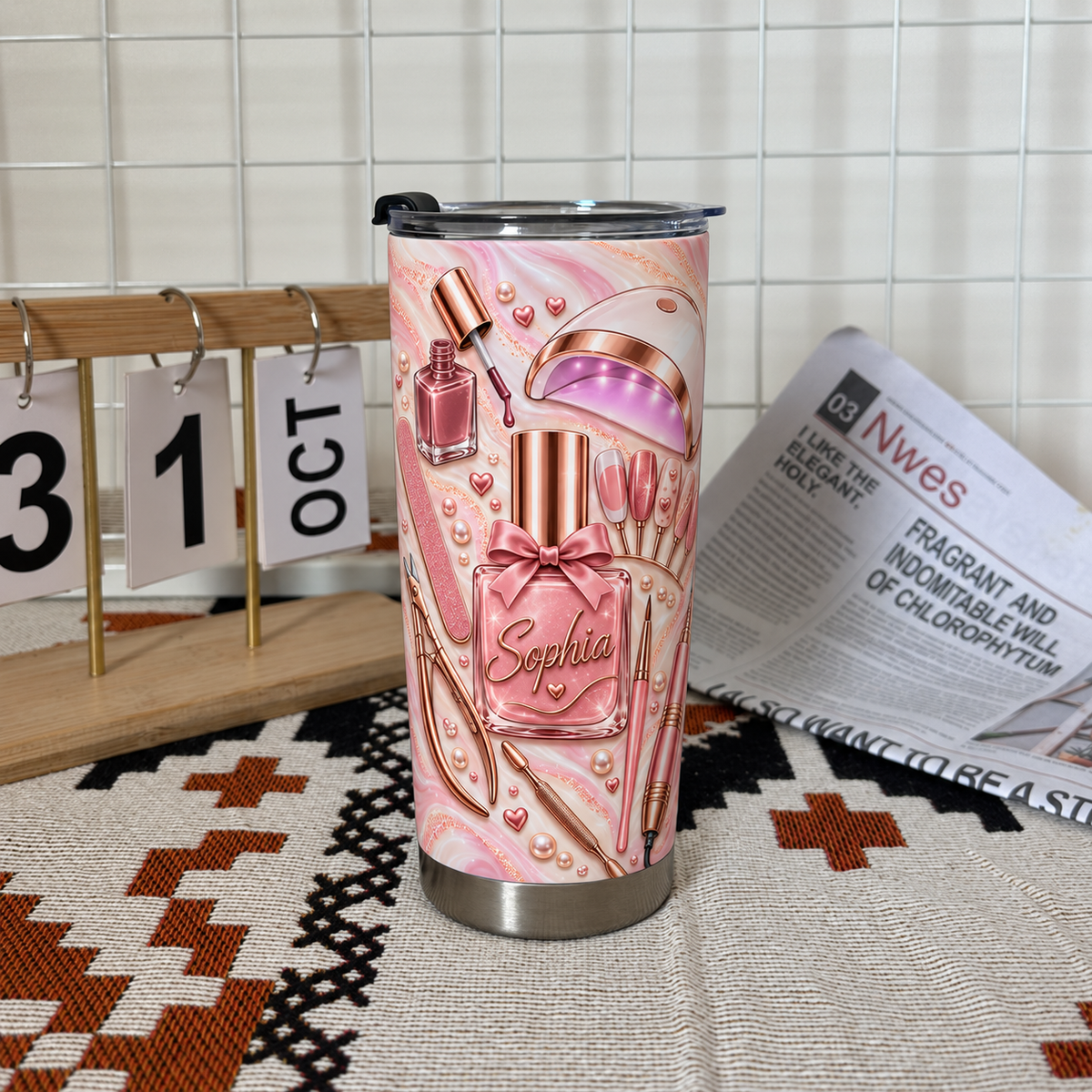 A personalized nail tech tumbler displayed on a woven mat next to a calendar grid and a folded newspaper backdrop.