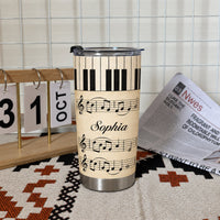 Personalized piano sheet music tumbler standing on a patterned mat next to a small wooden calendar and a newspaper on a white