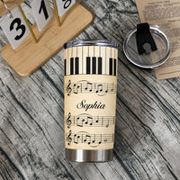 Personalized piano sheet music tumbler and lid resting on a dark rustic wooden surface next to a calendar block and