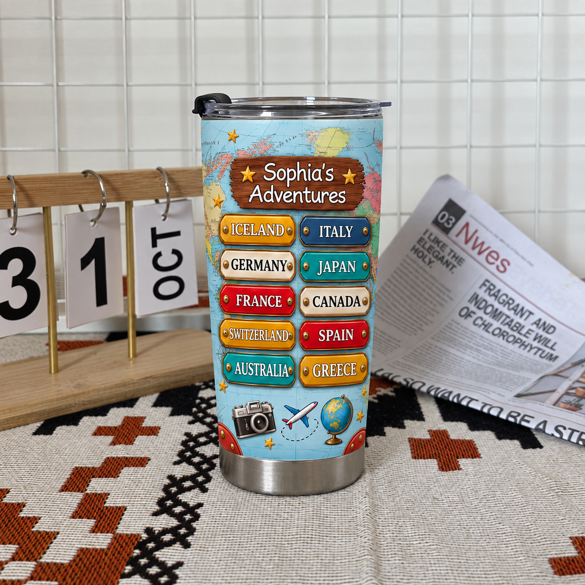 Stainless steel personalized travel map tumbler displayed with a calendar and newspaper on a textured mat.