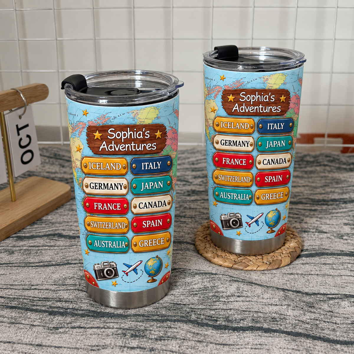 Two personalized travel map tumblers with world map design displayed together on a woven placemat.