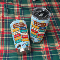 Two personalized travel map tumblers resting sideways on a red and green plaid fabric surface.