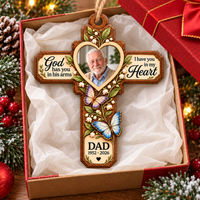 A Memorial Cross Wood Ornament placed inside an open gift box with tissue paper and holiday decorations.
