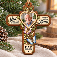 A Memorial Cross Wood Ornament hanging against a Christmas tree background with warm festive lights.