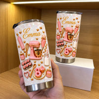 Hand holding a custom pink baking equipment collage tumbler in a wooden display