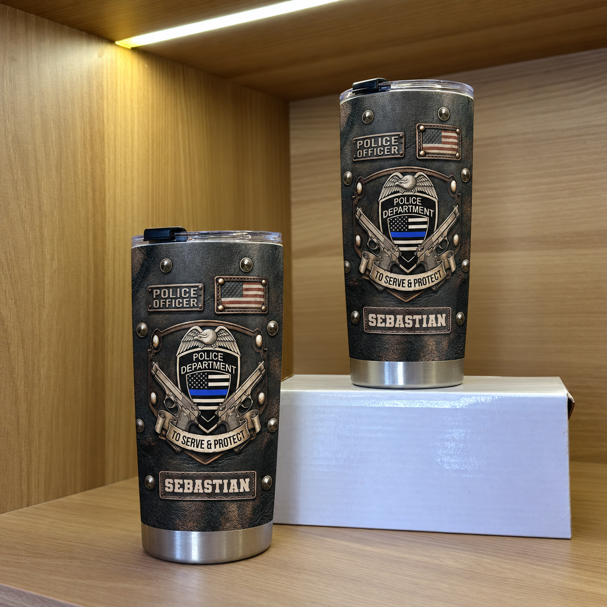 Two black faux-leather tactical drinkware tumblers featuring police badge and name, placed on a white box inside a wooden