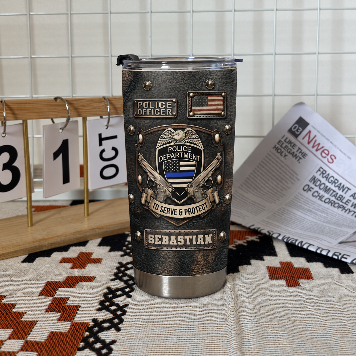 A single black faux-leather tumbler with thin blue line flag and police badge design standing on a patterned rug next to a