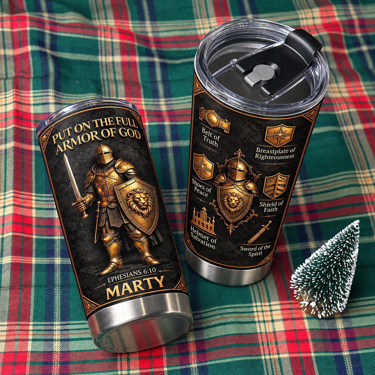 Two Full Armor Of God tumblers displayed upright on green plaid fabric next to small pine tree