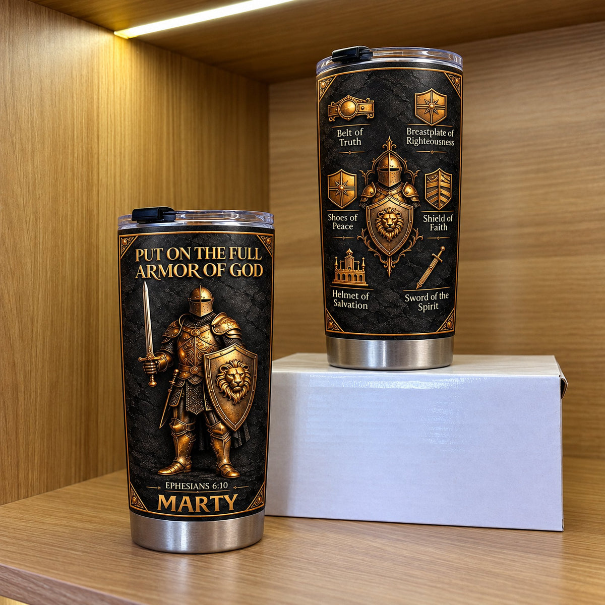 Two Full Armor Of God tumblers standing on small white box inside warm wooden shelf unit