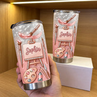 Hand holding a custom artist tumbler with pink glitter gradient on wooden shelf.