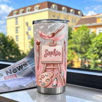 Rose Gold Artist Easel Tumbler displayed on a windowsill with a newspaper.