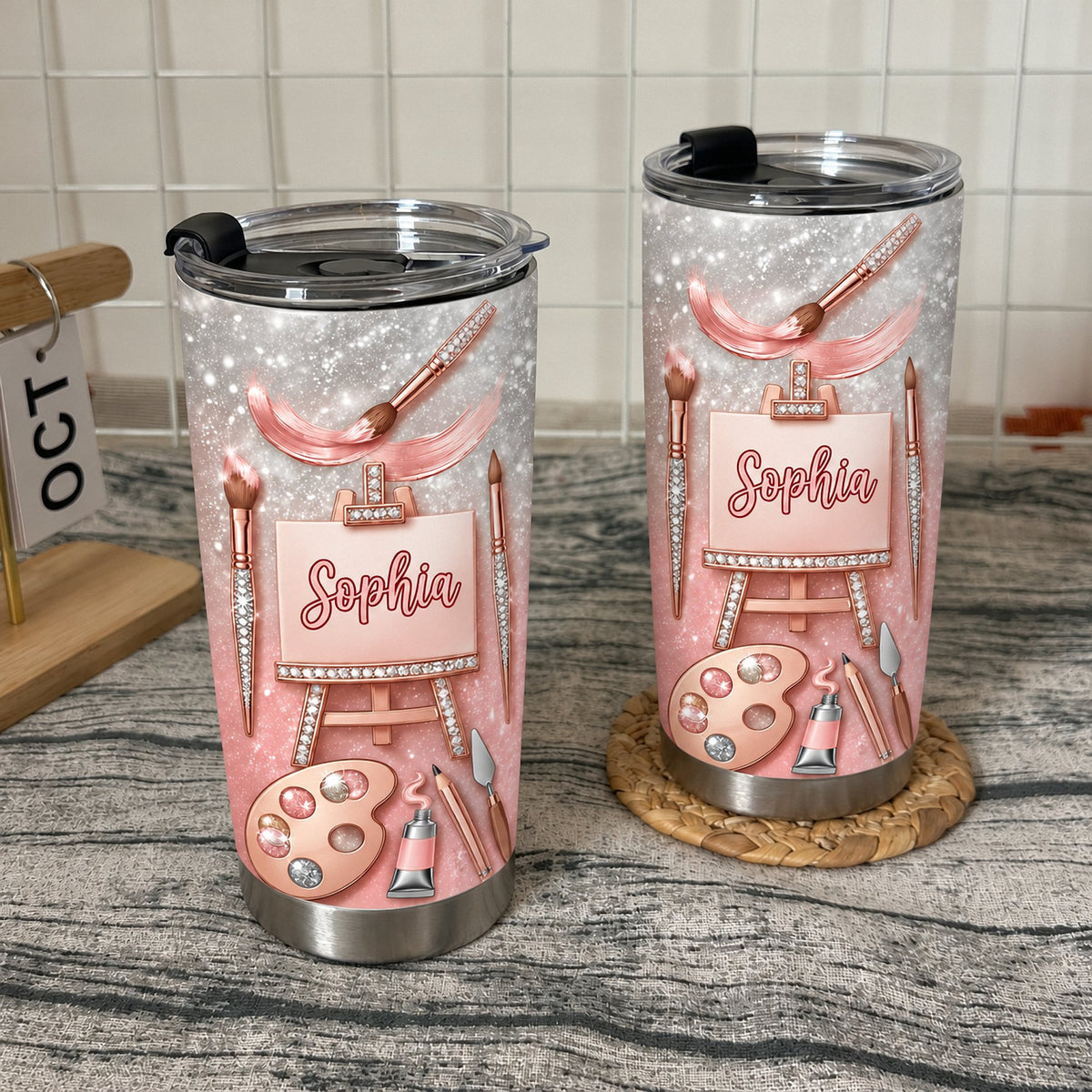 Two custom name artist tumblers standing on a textured surface with a small calendar.