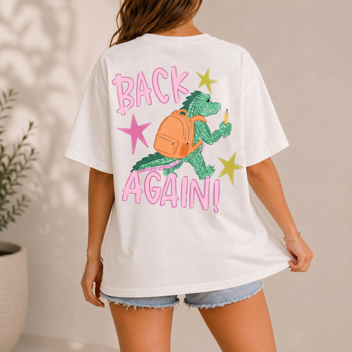 Woman wearing an off-white t-shirt showing the back view of an alligator graphic with backpack.