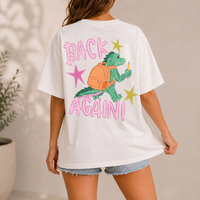 Woman wearing an off-white t-shirt showing the back view of an alligator graphic with backpack.