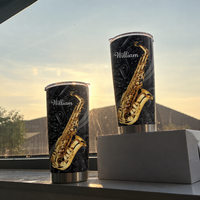 Two saxophone custom name tumblers sitting on a windowsill with a soft sunset sky and mountain view behind.