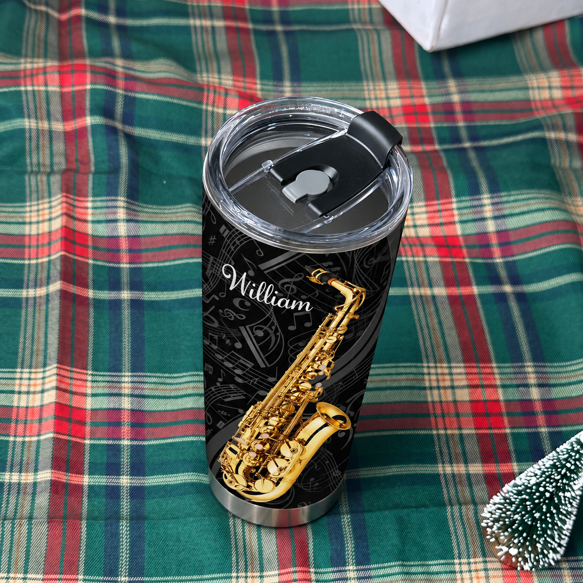 Insulated stainless steel saxophone tumbler with black background and golden jazz art resting on a green plaid blanket.