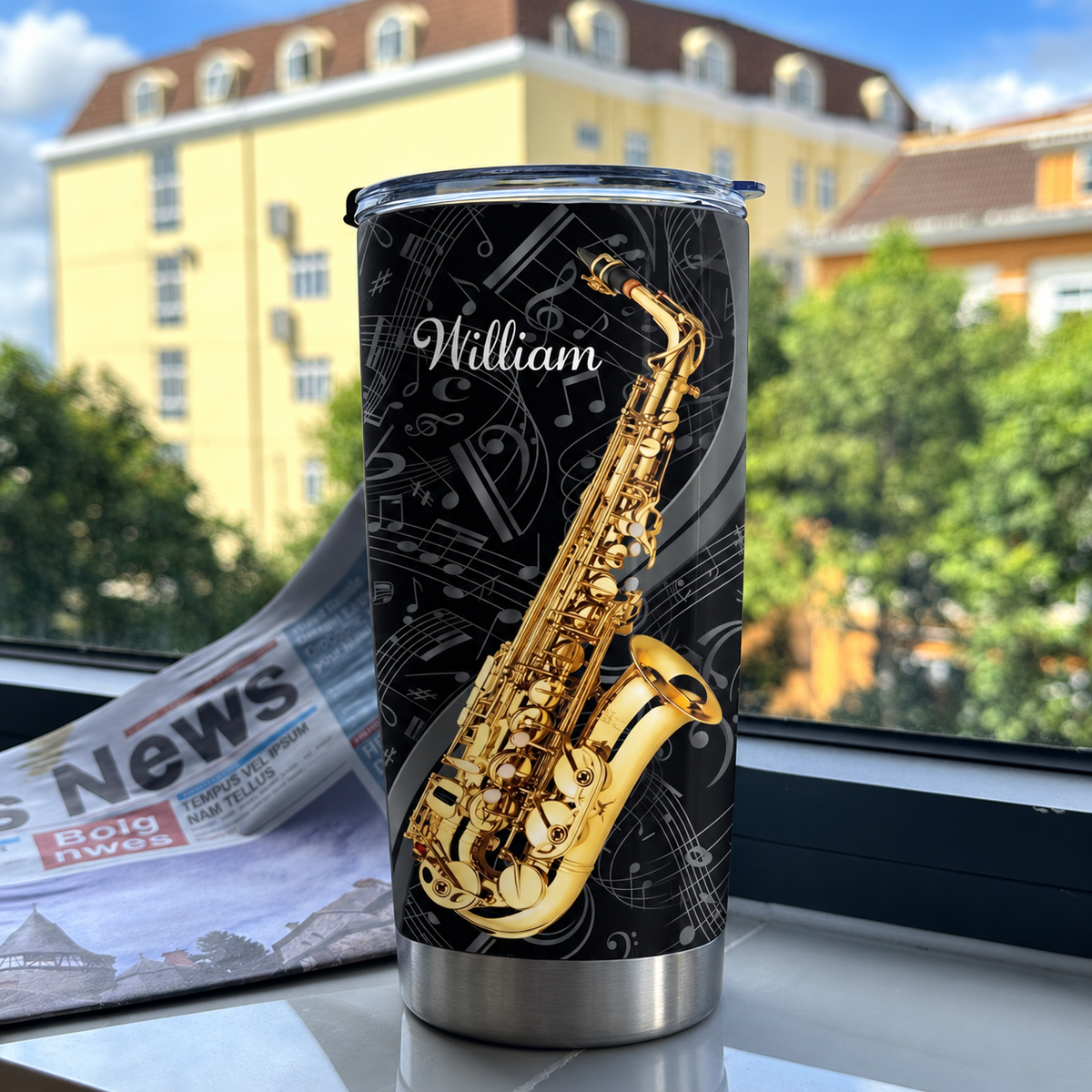 Custom saxophone tumbler with a black and gold design placed on a ledge in front of an open window and newspaper.